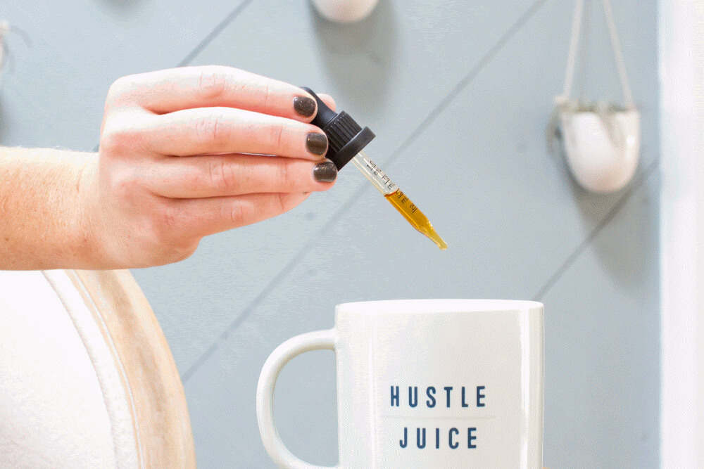 Person using eyedropper to add CBD oil to mug